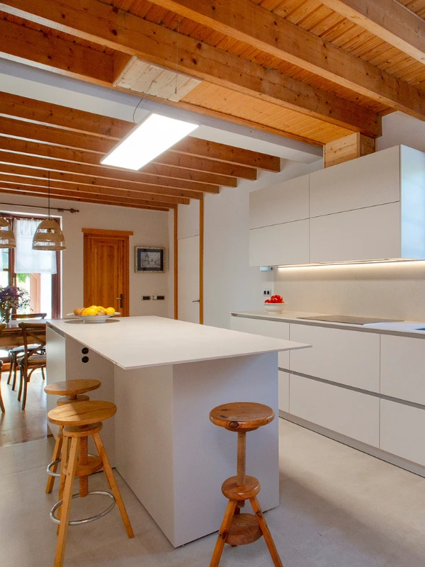 Isla de cocina clara con taburetes de madera, luminaria rectangular entre vigas y muebles Cashmere con iluminación LED