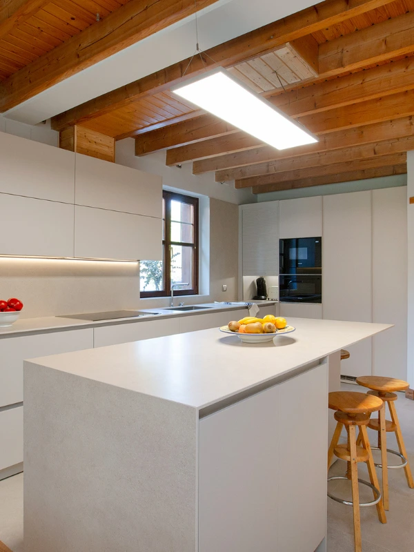 Isla de cocina en Cashmere con encimera en cascada y columnas con horno y microondas negros bajo vigas de madera