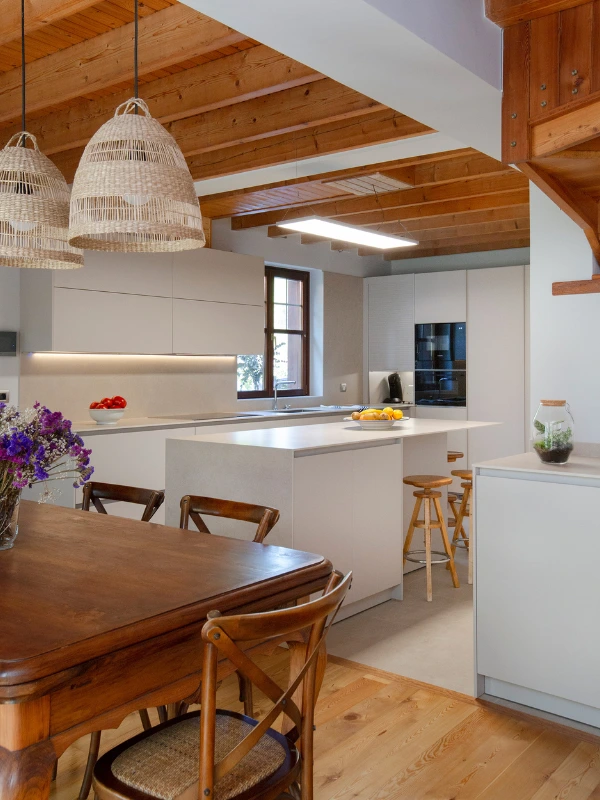 Cocina abierta Cashmere vista desde el comedor con mesa de madera, sillas de bistró y lámparas de fibra natural